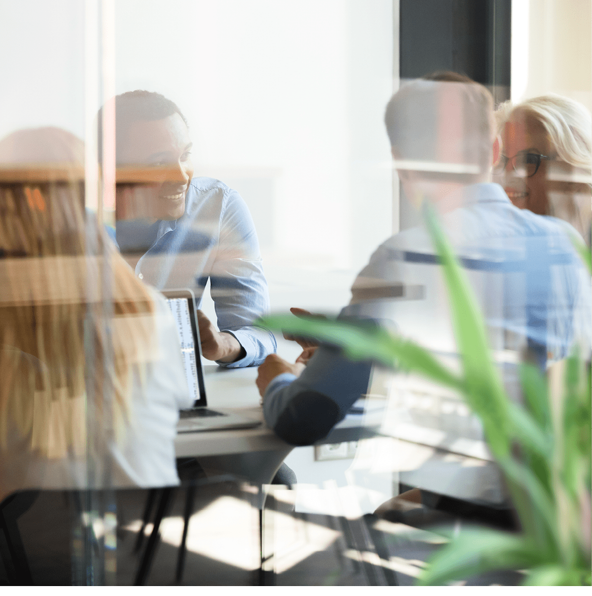 Multicultural international staff employees talking at team office company meeting sit at conference table behind glass door, diverse colleagues workers group collaborating at briefing in boardroom