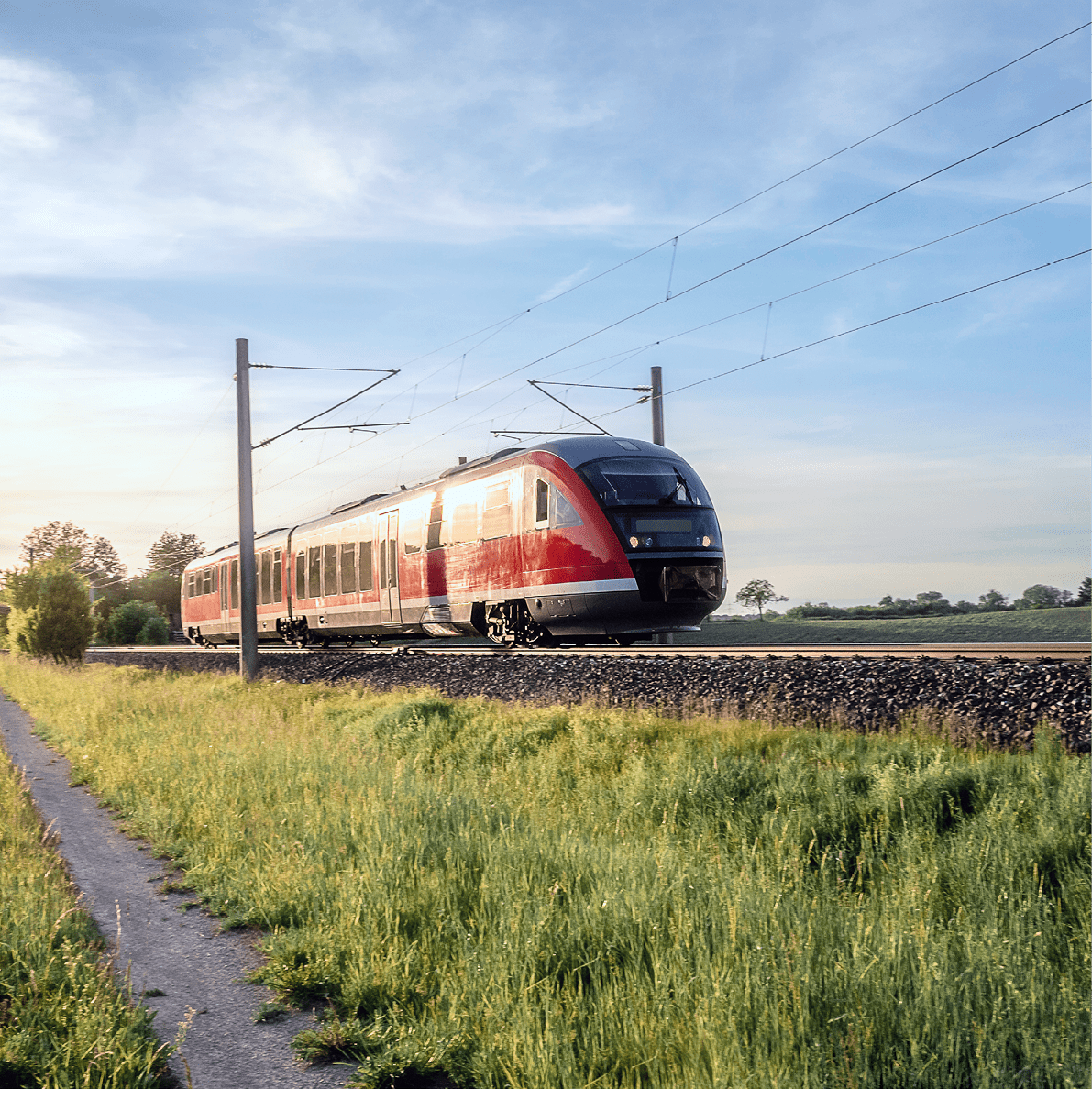 German train traveling through green fields on a sunny day of summer. Passenger train on rail tracks at sunset.