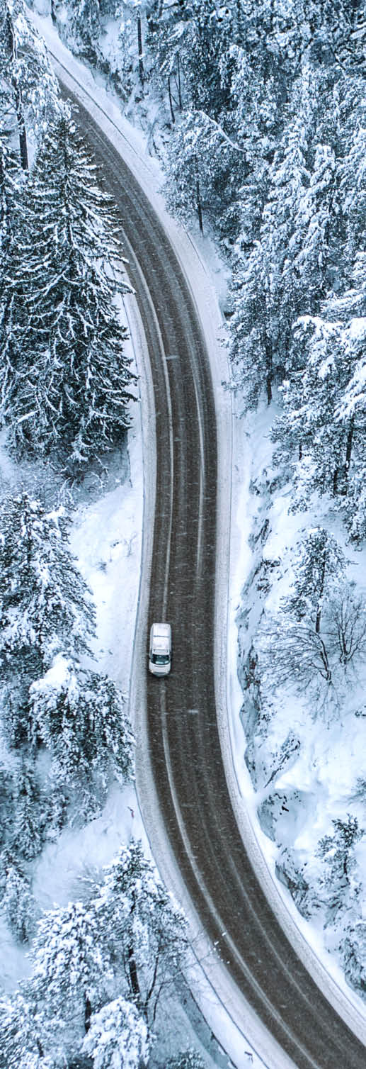 Winding, curving snowy mountain road in a pine forest with moving car during snowfall
