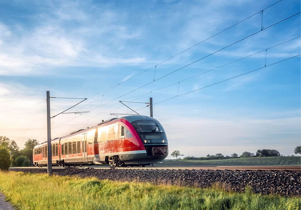 German train traveling through green fields on a sunny day of summer. Passenger train on rail tracks at sunset.
